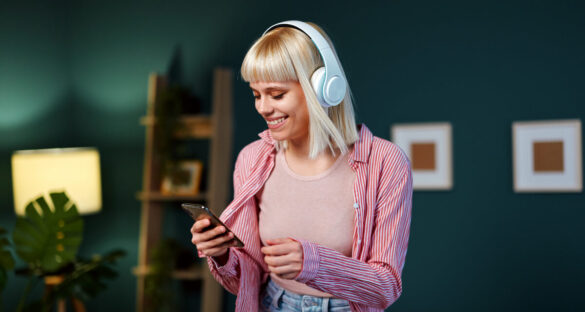 Uma jovem mulher caucasiana, vestindo roupas casuais, ouve podcasts de tecnologia em seu fone, na sala de casa.